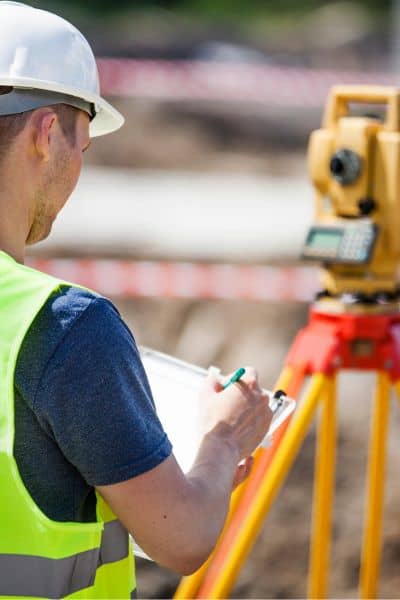 Land surveyor in safety vest using total station equipment during a construction staking survey at a building site in Houston
