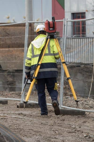 Licensed land surveyor conducting a boundary survey on a muddy site after heavy rain to verify property lines