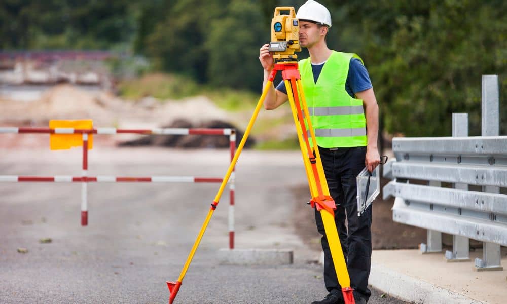 Surveyor performing a construction staking survey beside a highway project using a total station to measure elevations and set control points