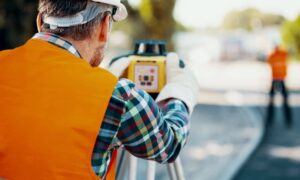 Land surveyor using a total station along a city street during redevelopment work for an ALTA Title Survey