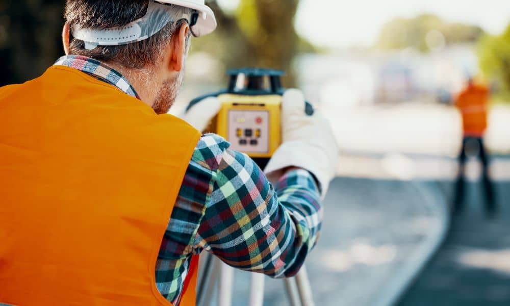 Land surveyor using a total station along a city street during redevelopment work for an ALTA Title Survey
