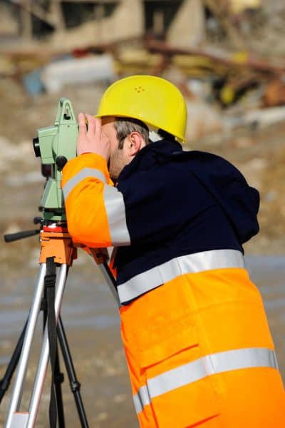 Professional land surveyor using a total station to collect boundary data for an ALTA Land Title Survey