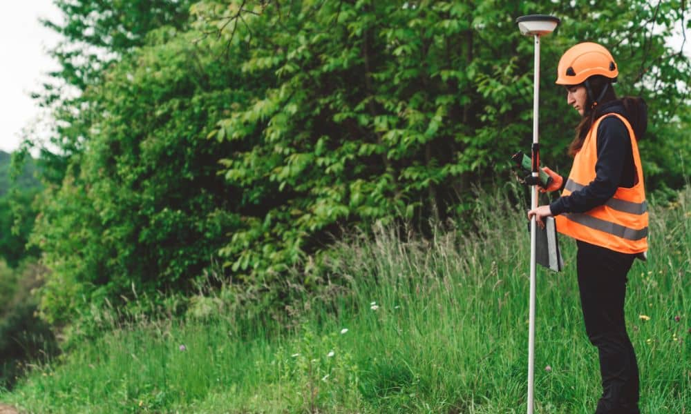 Surveyor using an RTK GPS rover during a topo survey on a grassy site near trees