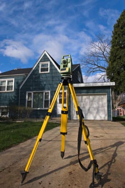 Surveying instrument set up on a tripod measuring property boundaries on a residential lot