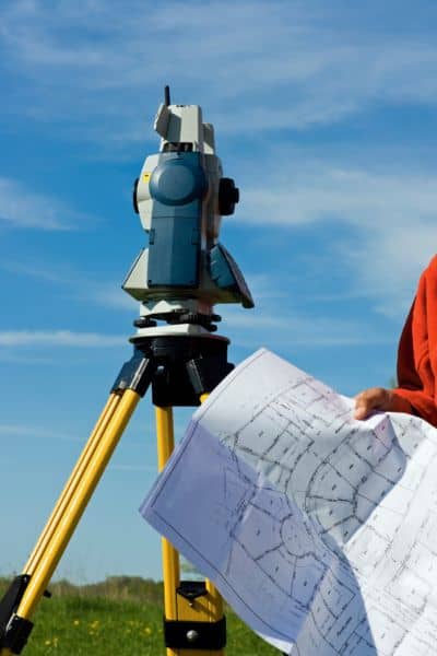 A licensed surveyor using a total station and reviewing a property map to verify property boundaries.
