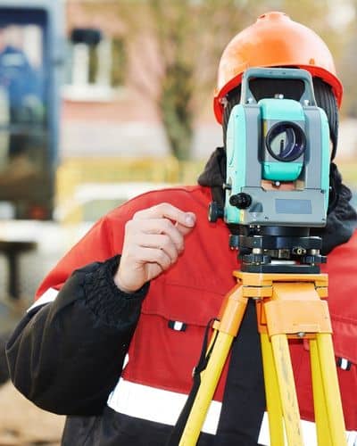 Land surveyor using tripod and total station equipment on a construction site during land surveying work